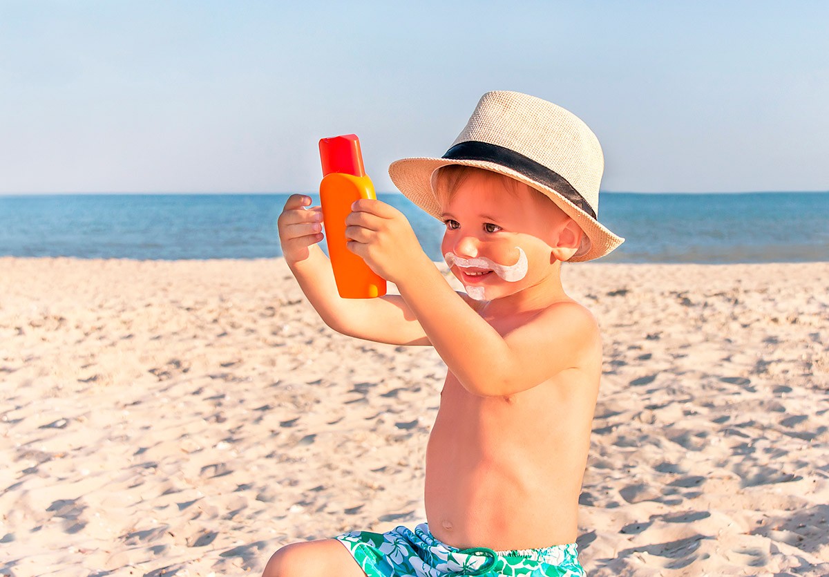 Enfant avec un chapeau tenant de la crème solaire sur la plage