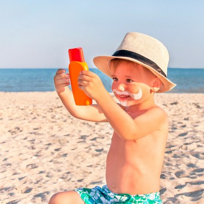 Enfant avec un chapeau tenant de la crème solaire sur la plage