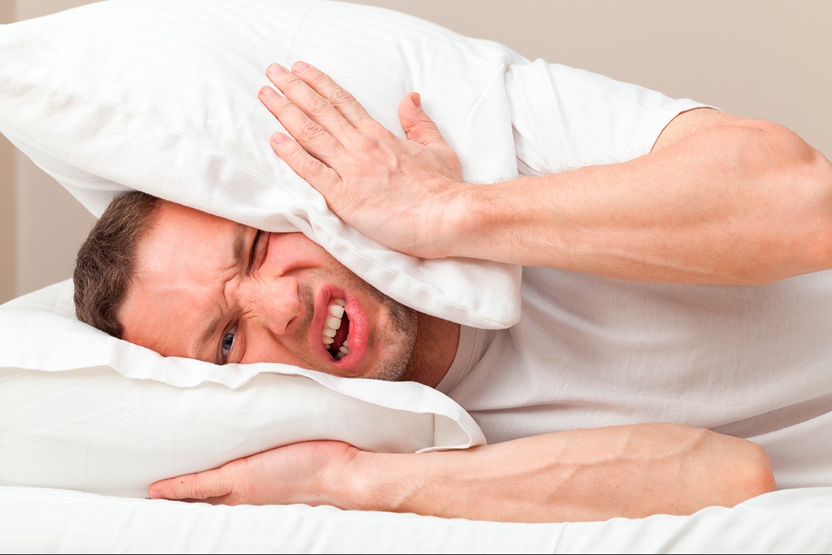 Homme allongé dans un lit se bouchant les oreilles avec un oreiller