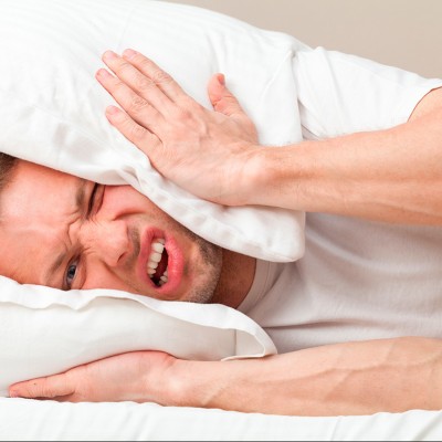 Homme allongé dans un lit se bouchant les oreilles avec un oreiller